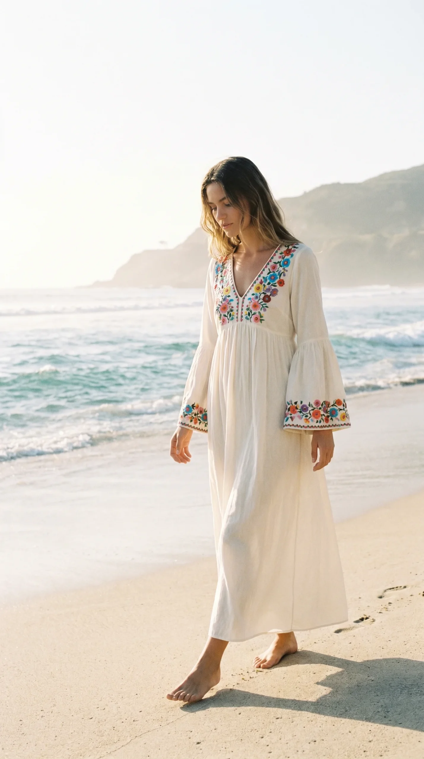 Woman in a flowy ivory cotton boho maxi dress with colorful embroidered floral detailing
