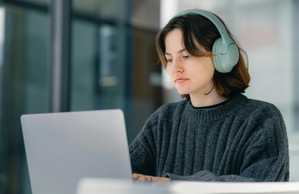 Woman wearing headphones while working at laptop using temptation bundling to beat procrastination